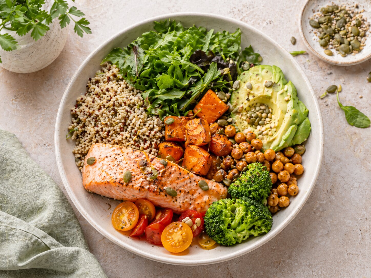 Сбалансированная миска с лососем, киноа, листовой зеленью, авокадо, нутом, брокколи и помидорами на светлой поверхности
